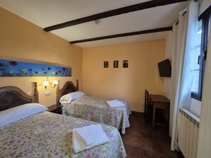 A hotel room with two beds, a desk, a chair, a painting, and a television on the wall.