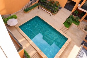 Ein Dachpool mit klar blauem Wasser, umgeben von einer beige gefliesten Liegefläche und einer kleinen Sitzgelegenheit mit einer Bank und einem Sonnenschirm.