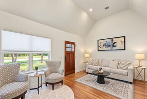 A living room with a sofa, two armchairs, a coffee table, a rug, and a painting on the wall.