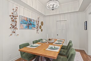 A dining room with a wooden table, green upholstered chairs, a chandelier, and wall art. - Charming MidTown Tulsa Home, w/Game Room,Walking Distance to Tulsa Expo Center (Tulsa)