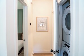 Un couloir avec une carte encadrée au mur, une porte donnant sur une chambre et un lave-linge dans un coin.