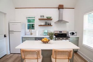 Une cuisine moderne avec des meubles blancs, une cuisinière en acier inoxydable, un four à micro-ondes et une fenêtre donnant sur un paysage verdoyant.