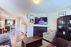 A modern living room with a fireplace, a television, and a dining area in the background. - Nolan Hill Retreat 3 BR Upper Level Home (Calgary)