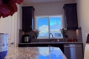 A kitchen with dark cabinets, a double sink, and a window with a view of a house. - Nolan Hill Retreat 3 BR Upper Level Home (Calgary)