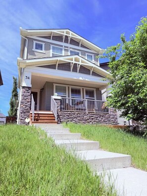 A two-story house with a stone facade, a front porch, and a staircase leading to the entrance. - Nolan Hill Retreat 3 BR Upper Level Home (Calgary)