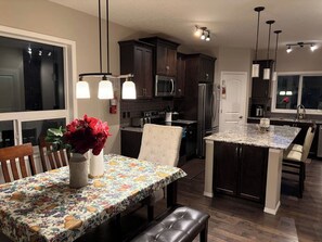 A modern kitchen with dark wood cabinets, stainless steel appliances, and a central island with seating. - Nolan Hill Retreat 3 BR Upper Level Home (Calgary)