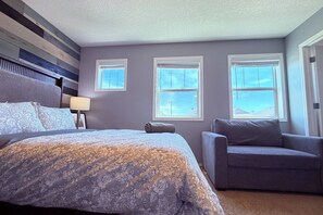 A bedroom with a bed, a chair, and three windows. - Nolan Hill Retreat 3 BR Upper Level Home (Calgary)