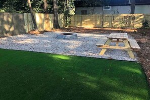 A backyard with artificial grass, a gravel area, a fire pit, and a wooden picnic table. - Magnolia House• Walk to FSU • Minutes to FAMU • Capitol • Midtown • Downtown (Tallahassee)