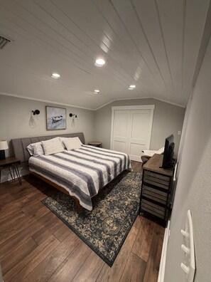Un dormitorio con cama, mesita de noche, lámpara y escritorio con computadora.