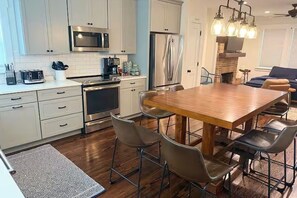 A modern kitchen with white cabinets, stainless steel appliances, a wooden dining table, and bar stools. - Magnolia House• Walk to FSU • Minutes to FAMU • Capitol • Midtown • Downtown (Tallahassee)