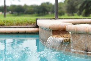 Una piscina amb una font, envoltada d'un marc de rajoles i una zona verda.