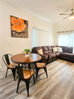 A living room with a sectional sofa, a round dining table with chairs, and a wall-mounted artwork. - Family Fun Getaway in Kissimmee! 4-Bedroom Retreat (Kissimmee)