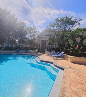 A swimming pool with a clear blue water feature, surrounded by lounge chairs and palm trees. - Family Fun Getaway in Kissimmee! 4-Bedroom Retreat (Kissimmee)