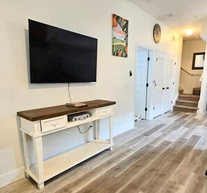 A living room with a flat-screen TV mounted on the wall, a wooden console table with drawers, and a herringbone-patterned floor. - Family Fun Getaway in Kissimmee! 4-Bedroom Retreat (Kissimmee)
