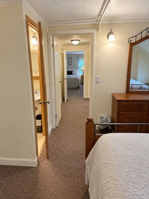 A hotel room with a bed, a dresser, a mirror, and a hallway leading to a bathroom and a bedroom. - Wiley Inn | Peaceful 2BR Retreat in the Green Mountains (Peru)