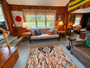 A cozy living room with a sofa, a patterned rug, and wooden walls. - Wiley Inn | Private Room in the Green Mountains (Peru)