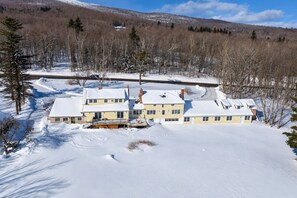 A two-story house with a snow-covered roof and a visible chimney, surrounded by a snowy landscape and trees. - Wiley Inn | Private Room in the Green Mountains (Peru)