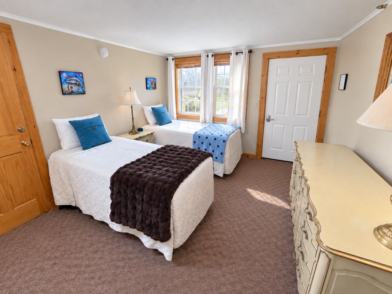 A bedroom with two beds, a dresser, and a window with curtains.