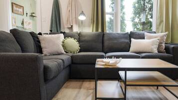 Un salon moderne avec un canapé d’angle, une table basse en bois et une vue sur l’extérieur grâce à de grandes fenêtres.