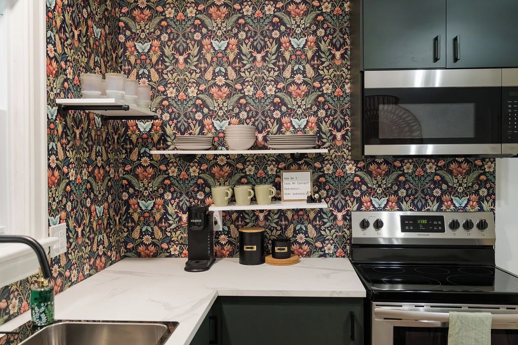 A kitchen with a floral wallpaper, a coffee maker, a microwave, and a stove.