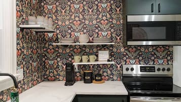 A kitchen with a floral wallpaper, a coffee maker, a microwave, and a stove.