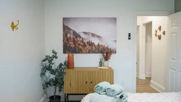 A bedroom with a bed, a wall-mounted painting, a potted plant, and a wooden cabinet.