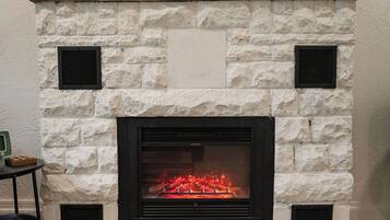 A stone fireplace with a fire, flanked by two vents, and a small table with a box on it to the left.