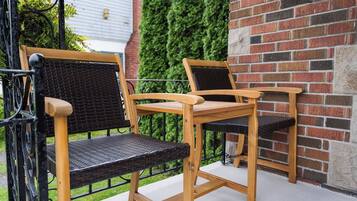 A wooden outdoor seating area with two chairs and a table, adjacent to a brick wall and a green ivy-covered wall.