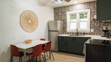 Une cuisine de taille réduite comprenant une table à manger, des chaises, un réfrigérateur et une fenêtre.
