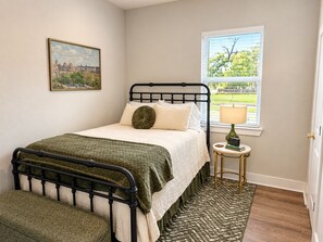 Een slaapkamer met een bed, een raam met zonwering, een nachtkastje met een lamp en een lijst met een afbeelding aan de muur.