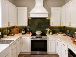 Una cocina moderna con armarios blancos, estufa de acero inoxidable y un salpicadero de azulejos verdes.