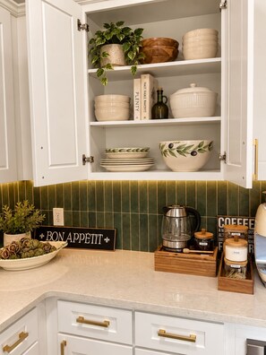 Una cocina con armarios blancos, un salpicadero de azulejos verdes y un letrero que dice 'BON APPETIT'.