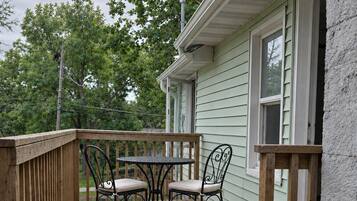 A wooden deck with a table and chairs, a railing, and a house in the background.