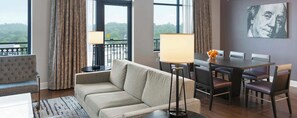 A modern living room with a sofa, dining table, chairs, and a view through large windows.