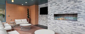 A modern lounge area with a brick wall, a flat-screen TV, a fireplace, and a seating arrangement including a sofa and two round tables.