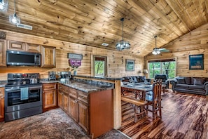 A wooden cabin interior with a kitchen, dining area, and living room. - Fox Den on Valley View - Hot tub & Fire pit (Pigeon Forge)
