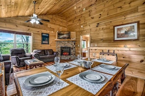 A wooden interior with a fireplace, dining table set for four, and leather seating. - Fox Den on Valley View - Hot tub & Fire pit (Pigeon Forge)