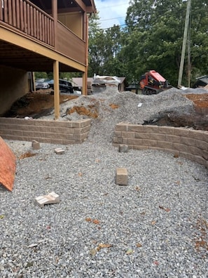 A construction site with gravel, brick walls, and a partially constructed building with a wooden balcony. - Fox Den on Valley View - Hot tub & Fire pit (Pigeon Forge)