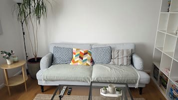 Ein Wohnzimmer mit einer Couch, einem Couchtisch, einem Bücherregal, einer Topfpflanze und einem kleinen Beistelltisch.