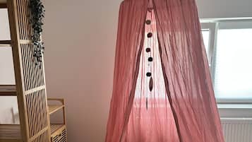 Una habitación con cama con dosel, un estante de madera con plantas y un ventanal.