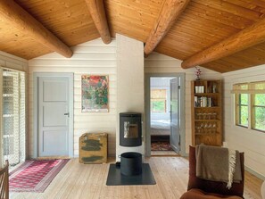 Ein gemütliches Zimmer mit Holzbalkendecke, Kamin, Bücherregal und einer Tür zu einem weiteren Raum.