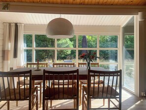 A dining area with a large table, chairs, and a hanging light fixture. - Renovated 1970s holiday home by the dunes (Nr. Nebel)