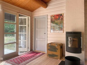 Ein Zimmer mit Holzboden, einer Tür, einem Fenster mit Vorhang, einem Plakat, einem Herd und einem Teppich.