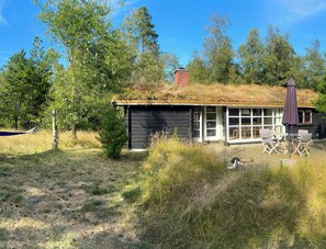 A cabin with a thatched roof, surrounded by trees and a grassy area. - Renovated 1970s holiday home by the dunes (Nr. Nebel)