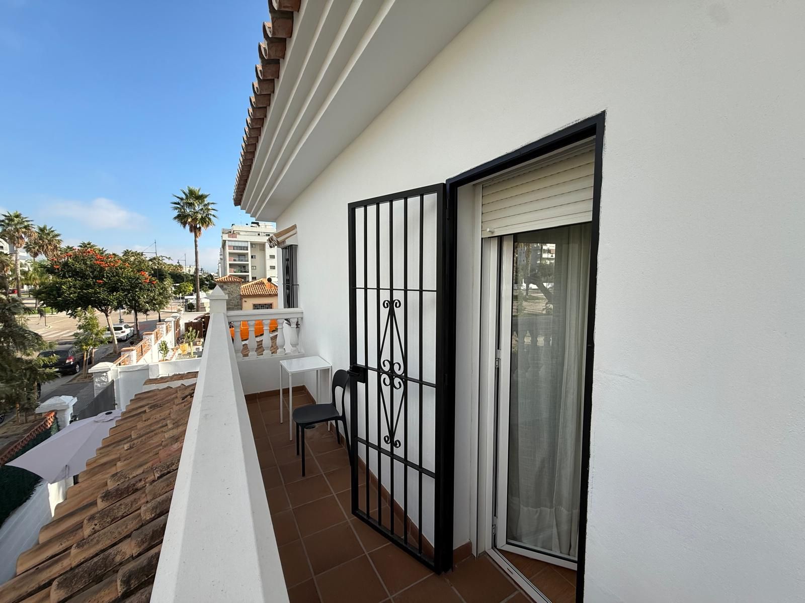 A balcony with a white railing, a sliding glass door, and a view of the street and neighboring buildings.