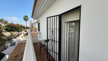 A balcony with a white railing, a sliding glass door, and a view of the street and neighboring buildings.
