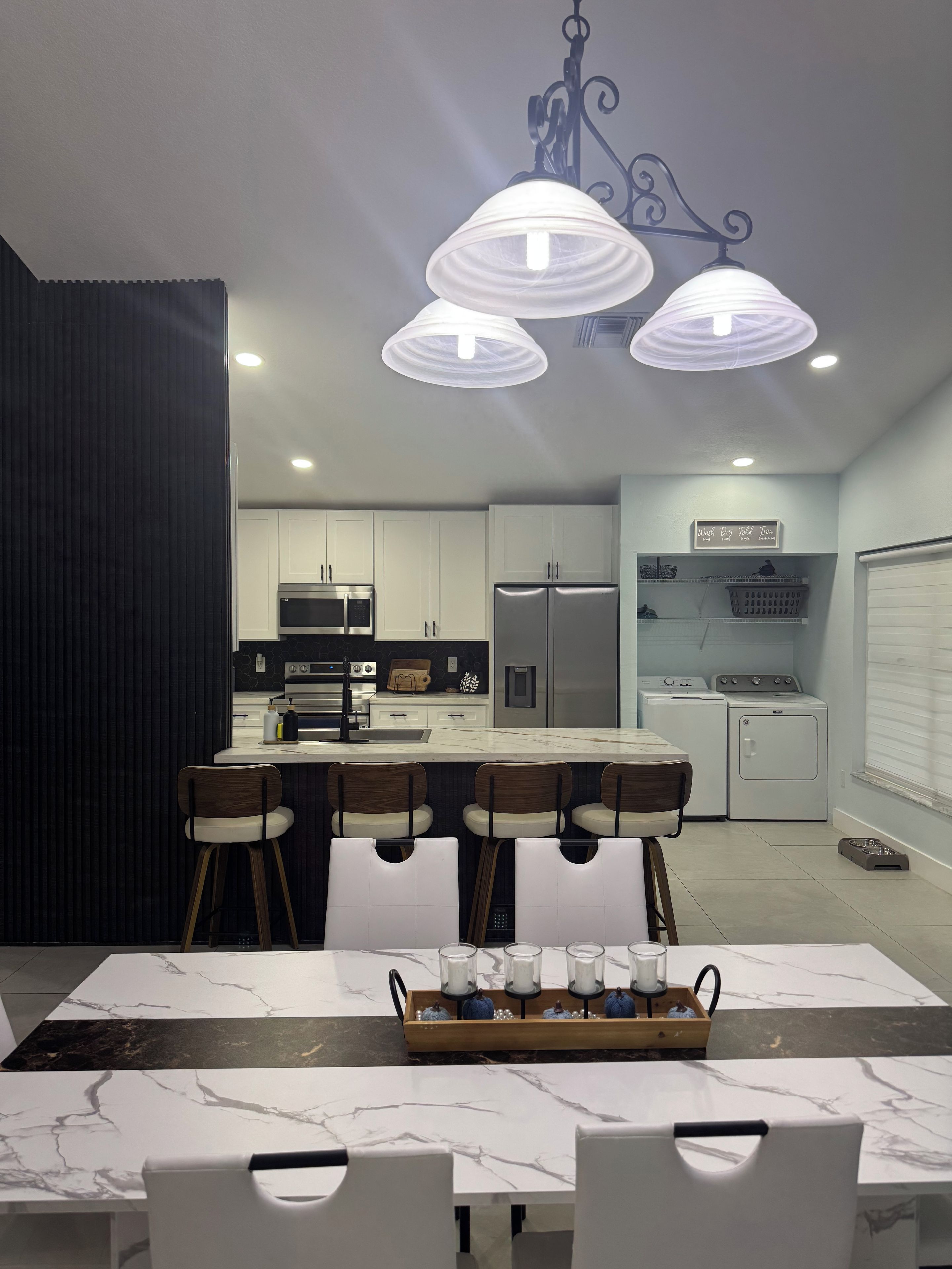 A modern kitchen with white cabinets, a central island with bar stools, a hanging light fixture, and a laundry area with a washing machine and dryer.