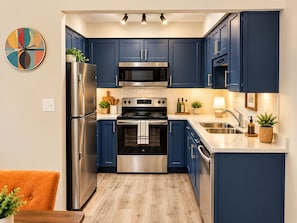 A modern kitchen with dark blue cabinets, stainless steel appliances, and a wooden floor. - 2-bedroom condo in fabulous Fenton, MI. (Fenton)