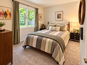 A bedroom with a bed, a nightstand, a dresser, a window with curtains, and a painting on the wall. - 2-bedroom condo in fabulous Fenton, MI. (Fenton)