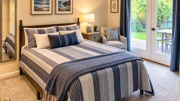 A bedroom with a large bed, a nightstand, a chair, a window with curtains, and a view of the outdoors.